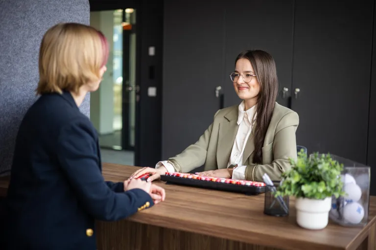 Oferty pracy | Uniwersytet WSB Merito Gdynia: Dwie kobiety siedzą przy biurku naprzeciwko siebie i załatwiają sprawy administracyjne