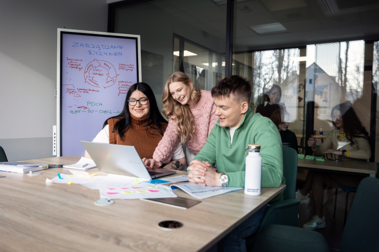 Kontynuuj studia | Uniwersytet WSB Merito Gdynia: Trójka studentów wspólnie uczy się w bibliotece. Używają laptopa. Za nimi znajduje się tablica z ich notatkami o zarządzaniu ryzykiem.
