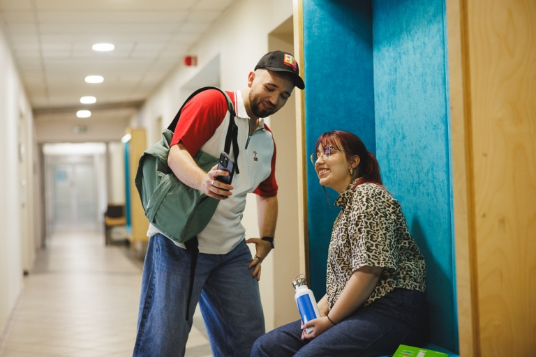 Nasz budynek | Uniwersytet WSB Merito Gdynia: Studentka na niebieskiej pufie i student na korytarzu Uniwersytetu WSB Merito Gdynia