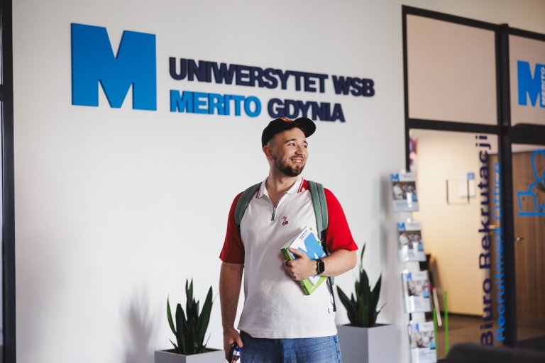 Rachunkowość i sprawozdawczość finansowa | Studia I stopnia w Gdyni | Uniwersytet WSB Merito Gdynia: Student na korytarzu przy logo Uczelni