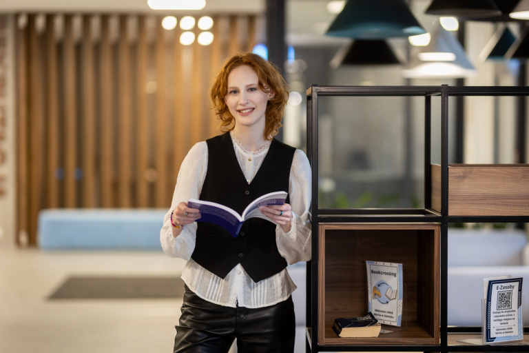 Akademia menedżera | Studia podyplomowe w Gdyni | Uniwersytet WSB Merito Gdynia: Studentka w holu przy półce z książką w ręku