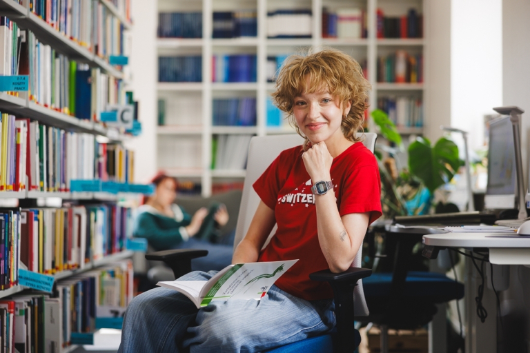 Zarządzanie nieruchomościami i pośrednictwo | Studia I stopnia w Gdyni | Uniwersytet WSB Merito Gdynia: Studentka w bibliotece z książką na kolanach