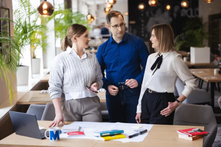 Rozmowa trzech osób stojących przy biurku, omawiają jakiś projekt