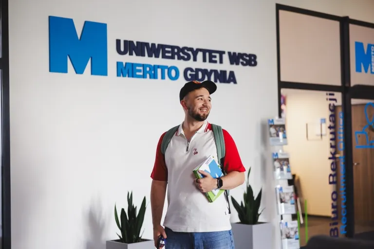 Student na korytarzu przy logo Uczelni