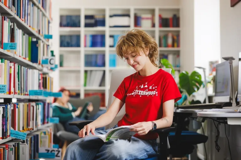Biblioteka zaprasza: spotkanie autorskie z Alicją Balcerzak | Aktualności | Uniwersytet WSB Merito Gdynia: Studentka w bibliotece przegląda książkę 