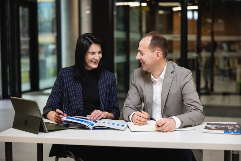 Studia MBA i EMBA | Uniwersytet WSB Merito: uczestnicy MBA w Poznaniu siedzą przy stole z laptopem i informatorem- Uniwersytety WSB Merito