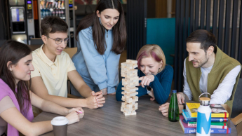 Logistics | Uniwersytet WSB Merito Łódź: Grupa pięciu młodych osób gra w Jengę przy okrągłym stole w przyjaznej, nieformalnej atmosferze, skupiona na ruchu jednej z uczestniczek.