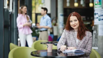 Digital marketing | Studia II stopnia w Łodzi | Uniwersytet WSB Merito Łódź: Studentka zapisuje notatki, a obok stoi kawa.