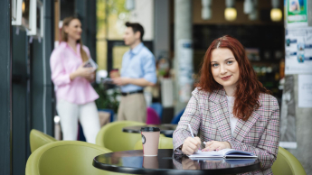 Digital marketing | Studia II stopnia ze studiami podyplomowymi  | Uniwersytet WSB Merito Łódź: Studentka zapisuje notatki, a obok stoi kawa.