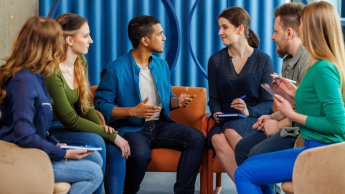 Język niemiecki w komunikacji biznesowej | Uniwersytet WSB Merito Łódź: Grupa studentów dyskutuje, siedząc na kanapach.