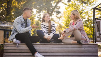 Grupa studentów rozmawia na ławce w plenerze.