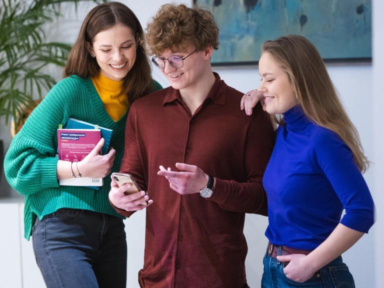 Organizacje i koła naukowe | Uniwersytet WSB Merito Łódź: Trzech studentów ogląda telefon chłopaka po środku