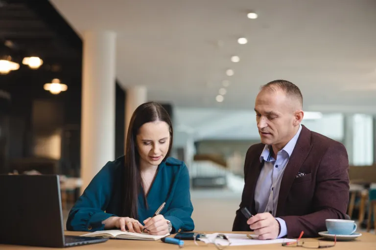 Gospodarowanie nieruchomościami | Studia I stopnia w Łodzi | Uniwersytet WSB Merito Łódź: Kobieta i mężczyzna siedzą przy stole w nowoczesnym wnętrzu, wspólnie analizując notatki i dokumenty.