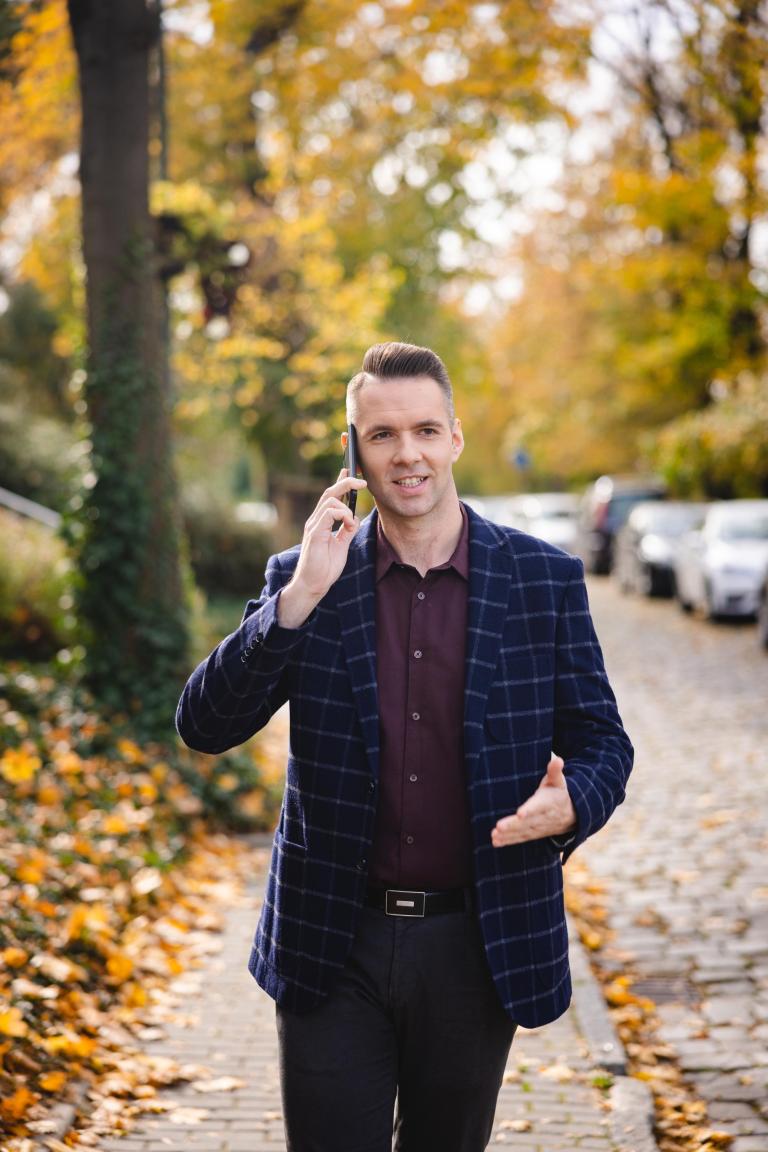 Psychologia w zarządzaniu | Studia II stopnia ze studiami podyplomowymi  | Uniwersytet WSB Merito Łódź: Mężczyzna w marynarce rozmawia przez telefon, idąc jesienną ulicą.