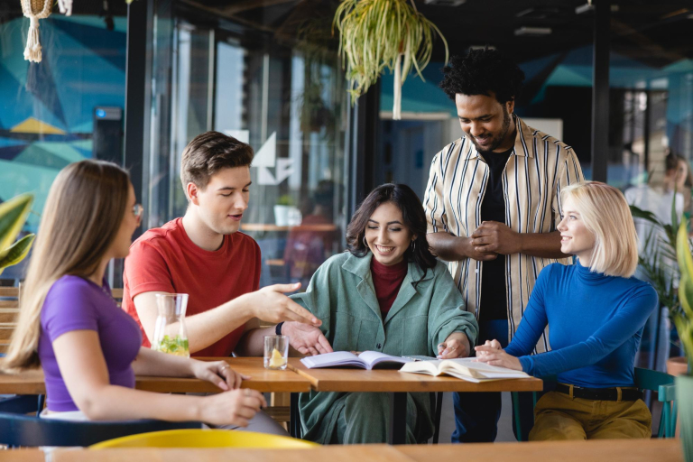 SAP S/4 HANA – Nowoczesny system ERP | Studia podyplomowe w Łodzi | Uniwersytet WSB Merito Łódź: Piątka studentów siedzi przy stole i dyskutuje nad książką.