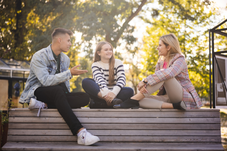 Prawo dla menedżera, studia podyplomowe: Grupa studentów rozmawia na ławce w plenerze.