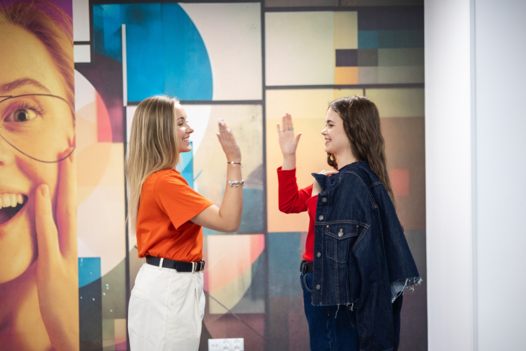 SAP Finance & Controlling Masterclass | Studia podyplomowe w Łodzi | Uniwersytet WSB Merito Łódź: Dwie młode kobiety uśmiechnięte przybijają piątkę.