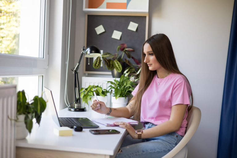 AI – uniwersalne kompetencje jutra | Studia podyplomowe w Łodzi | Uniwersytet WSB Merito Łódź: Studentka siedzi przy biurku i przygotowuje się do zajęć