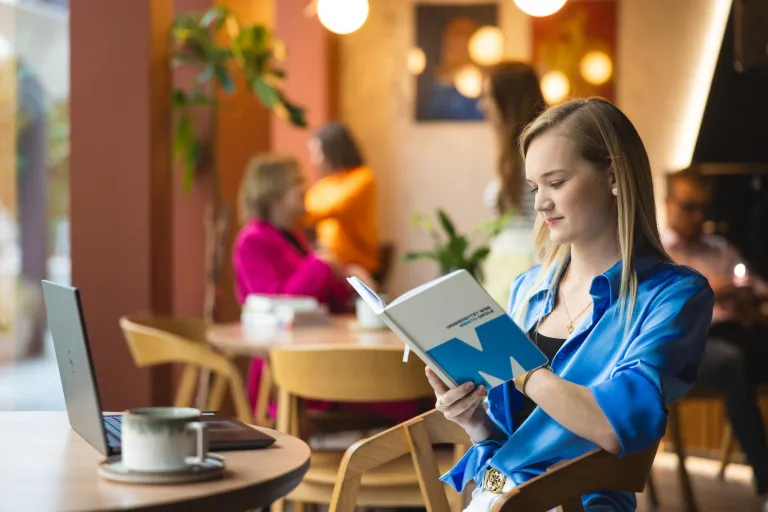 Management | Studia I stopnia w Łodzi | Uniwersytet WSB Merito Łódź: Dziewczyna w kawiarni przegląda notatnik.