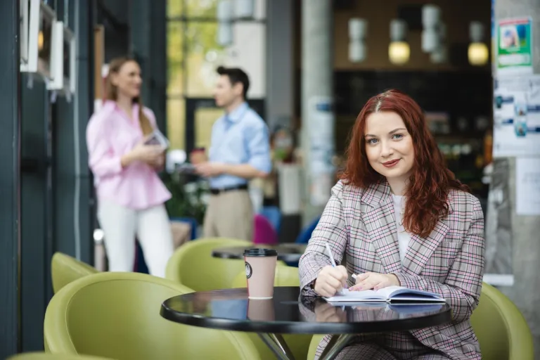 Projektowanie komunikacji i doświadczeń marki | Studia II stopnia ze studiami podyplomowymi  | Uniwersytet WSB Merito Łódź: Studentka zapisuje notatki, a obok stoi kawa.