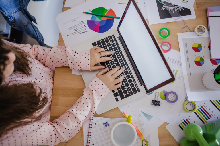 Psychologia reklamy i komunikacji | Studia podyplomowe w Opolu | Uniwersytet WSB Merito Opole: Kobieta pisze na komputerze wśród kartek z wykresami