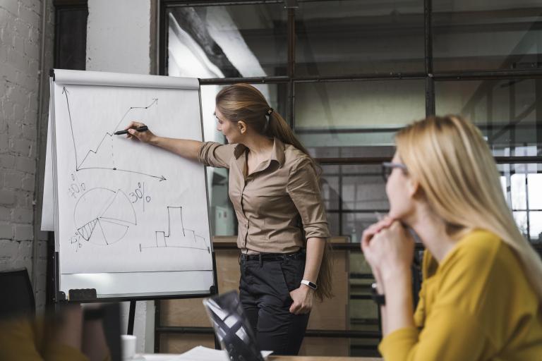 Zarządzanie i inwestowanie w nieruchomości | Studia podyplomowe w Opolu | Uniwersytet WSB Merito Opole: Kobieta wskazuje na wykres liniowy przed inną osobą