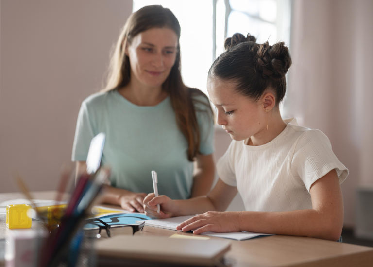 Psychologia edukacyjna | Studia podyplomowe w Opolu | Uniwersytet WSB Merito Opole: Dziecko pisze w zeszycie, obok siedzi dorosła kobieta