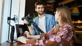 Media i komunikacja w biznesie | Studia I stopnia w Opolu | Uniwersytet WSB Merito Opole: Zdjęcie główne: Opole - Media i komunikacja w biznesie - dziewczyna i chłopak rozmawiają, chłopak ma w ręce aparat  fotograficzny