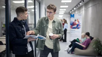 Bezpieczeństwo i higiena pracy | Studia I stopnia w Opolu | Uniwersytet WSB Merito Opole: Główna grafika: Opole - Bezpieczeństwo i higiena pracy  - studenci stojący na korytarzu, przeglądają notatki