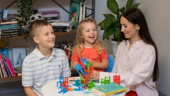 Praca z osobami niedostosowanymi społecznie z profilaktyką uzależnień | Studia I stopnia w Opolu | Uniwersytet WSB Merito Opole: Główna grafika: Opole - specjalność: Praca z osobami niedostosowanymi społecznie z profilaktyką uzależnień - siedząca przy stole kobieta z dwójką dzieci, podczas zabawy rysunkowej 