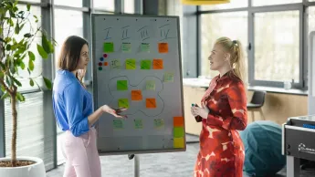 Social media i influencer marketing | Studia podyplomowe w Opolu | Uniwersytet WSB Merito Opole: Główna grafika: Opole - studia podyplomowe - Social media i influencer marketing - Dwie kobiety stojące przy białej tablicy, tworzą notatki