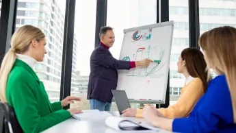 Zarządzanie jakością w branży automotive | Studia podyplomowe w Opolu | Uniwersytet WSB Merito Opole: Główna grafika: Opole - studia podyplomowe - Zarządzanie jakością w branży automotive - grupa osób słuchająca wypowiedzi mężczyzny stojącego przy tablicy