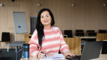 Kadry i płace | Studia podyplomowe w Opolu | Uniwersytet WSB Merito Opole: Główna grafika: Opole - studia podyplomowe - Kadry i płace - Kobieta siedząca za biurkiem, tworzy notatki, przed nią stoi laptop