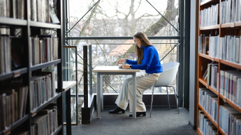 Zarządzanie i automatyzacja procesów w administracji publicznej | Studia podyplomowe w Opolu | Uniwersytet WSB Merito Opole: Główna grafika: Opole - studia podyplomowe - Zarządzanie i automatyzacja procesów w administracji publicznej - Kobieta siedząca w bibliotece, korzysta z laptopa