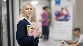 Kosmetologia anti-aging | Studia I stopnia w Opolu | Uniwersytet WSB Merito Opole: Główna grafika: Opole - studia I stopnia - specjalność Kosmetologia anti-aging - Dziewczyna stojąca na korytarzu, trzyma pod ręką książki
