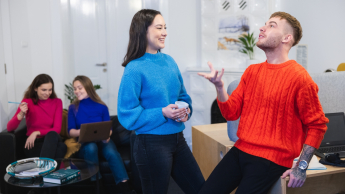 Pedagogika szkolna z doradztwem zawodowym | Uniwersytet WSB Merito Opole: Główna grafika: Opole - studia II stopnia - specjalność Pedagogika szkolna z doradztwem zawodowym - Dwie rozmawiające osoby, chłopak podrzuca w dłoni żółtą piłkę, w tle siedzą dwie dziewczyny i patrzą w ekran laptopa