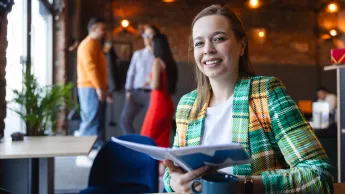 Digital marketing | Studia II stopnia w Opolu | Uniwersytet WSB Merito Opole: Główna grafika: Opole - studia II stopnia - specjalność Digital marketing -Kobieta trzymająca w dłoniach otwarty notatnik z logotypem Uniwersytetu WSB Merito