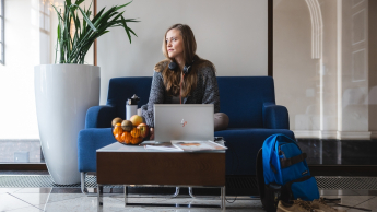 Nutripsychiatria | Uniwersytet WSB Merito Opole: Główna grafika: Opole - studia podyplomowe - Nutripsychiatria - Kobieta siedząca na niebieskiej kanapie, korzysta z laptopa