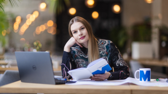 Psychoneuroimmunologia (PNI) | Uniwersytet WSB Merito Opole: Główna grafika: Opole - studia podyplomowe - Psychoneuroimmunologia (PNI) - Kobieta siedząca przy biurku, trzyma w dłoni otwarty notes