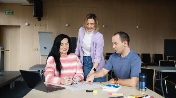 Warsztat pracy pedagoga-wychowawcy | Studia podyplomowe w Opolu | Uniwersytet WSB Merito Opole: Główna grafika: Opole - studia podyplomowe - Event Manager - uczestnicy analizują treść przy stole w sali budynku uczelni