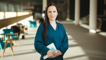 Zarządzanie finansami w przedsiębiorstwie | Studia podyplomowe w Opolu | Uniwersytet WSB Merito Opole: Główna grafika: Opole - studia podyplomowe -Zarządzanie finansami w przedsiębiorstwie- uczestniczka studiów podyplomowych stoi w korytarzu biblioteki z książką w ręce