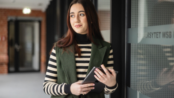 MBA HR | Studia MBA w Opolu | Uniwersytet WSB Merito Opole: Uczestniczka studiów podyplomowych stoi i opera się plecami o półkę w bibliotece, trzymając w ręce książki