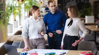 Analiza i informatyka śledcza | Uniwersytet WSB Merito Opole: Główna grafika: Opole - studia podyplomowe - Analiza i informatyka śledcza- uczestnicy studiów podyplomowych stoją przy biurku i rozmawiają