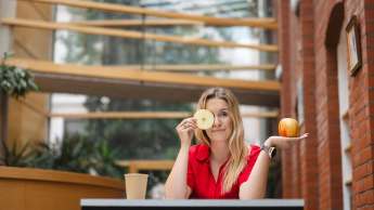 Neurodietetyka | Studia podyplomowe w Opolu | Uniwersytet WSB Merito Opole: Główna grafika: Opole - studia podyplomowe- Neurodietetyka- uczestniczka studiów podyplomowych siedzi przy biurku z jabłkiem w ręce