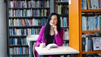 Warsztat pracy pedagoga-wychowawcy | Studia podyplomowe w Opolu | Uniwersytet WSB Merito Opole: Główna grafika: Opole - studia podyplomowe -Warsztat pracy pedagoga-wychowawcy- uczestniczka studiów podyplomowych siedzi przy stoliku i robi notatki