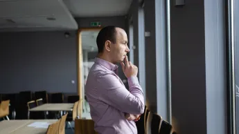 Zarządzanie i automatyzacja procesów w biznesie | Studia podyplomowe w Opolu | Uniwersytet WSB Merito Opole: Główna grafika: Opole - studia podyplomowe -Zarządzanie i automatyzacja procesów w biznesie- uczestnik studiów podyplomowych stoi oparty o stół i patrzy przez okno