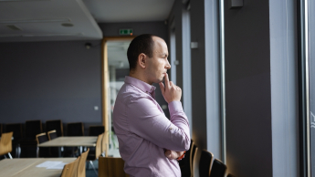 Księgowość i płace w przedsiębiorstwie | Uniwersytet WSB Merito Opole: Główna grafika-Opole- studia podyplomowe- Wykorzystanie zarządzania kryzysowego, obrony cywilnej i cyberbezpieczeństwa w planowaniu i zapobieganiu atakom terrorystycznym - uczestnik studiów podyplomowych stoi, opierając się o biurko i rozmyśla spoglądając za okno 