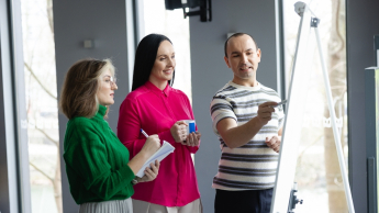 Psychodietetyka  dzieci i młodzieży | Studia podyplomowe w Opolu | Uniwersytet WSB Merito Opole: Główna grafika: Opole - studia podyplomowe -Psychodietetyka dzieci i młodzieży - uczestnicy studiów podyplomowych stoją i analizują wspólnie treści na flipcharcie