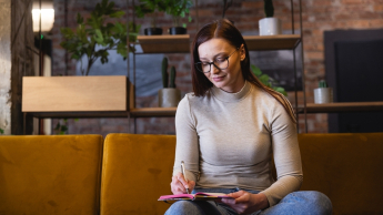 Diversity and Inclusion - Zarządzanie różnorodnością w organizacji | Studia podyplomowe w Opolu | Uniwersytet WSB Merito Opole: Główna grafika: Opole - studia podyplomowe -Diversity and Inclusion - Zarządzanie różnorodnością w organizacji - uczestniczka studiów podyplomowych siedzi na kanapie i piszę w notatniku