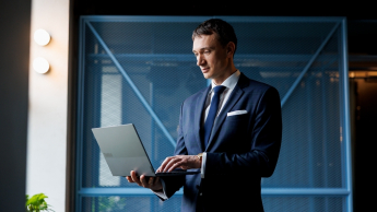 Inżynieria oprogramowania w JavaScript (TypeScript) | Studia podyplomowe w Opolu | Uniwersytet WSB Merito Opole: Główna grafika:Opole - studia podyplomowe - Inżynieria oprogramowania w JavaScript (TypeScript) - uczestnik studiów podyplomowych stoi z otwartym laptopem w rękach 